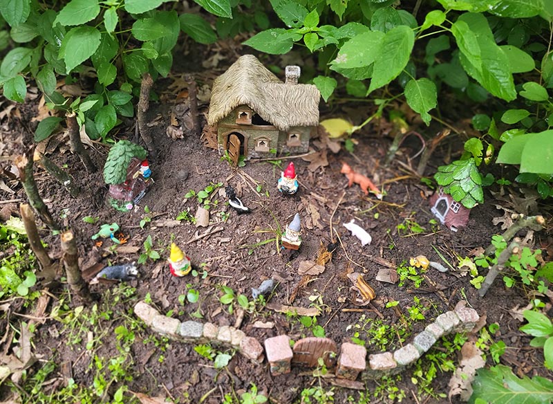 A miniature elf village in the woods — a thatched cottage, stone garden wall, gnomes and small animals among the leaves