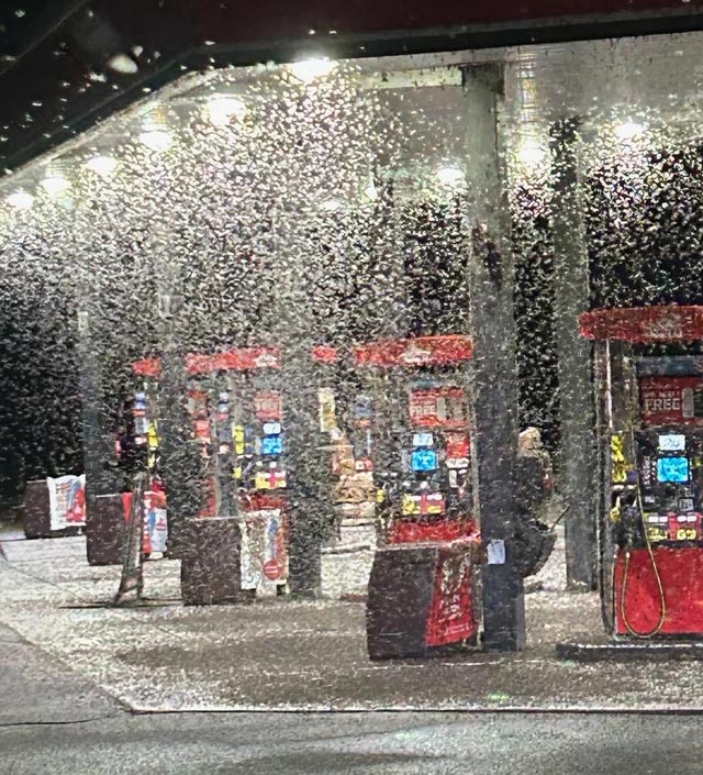 A swarm of mayflies covering the lights and pumps at a gas station at night